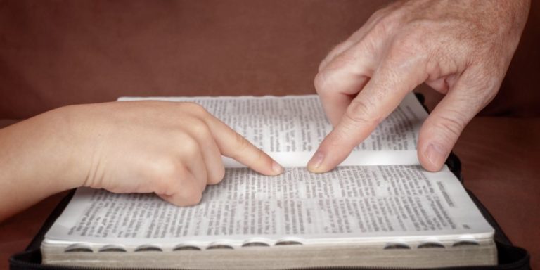 two hands pointing at words in bible